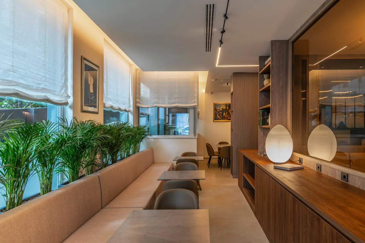 sala dell'hotel con panca, tavoli, piante lungo le finestre e bancone in legno