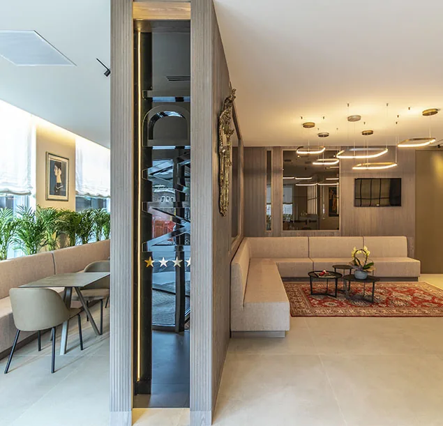 hall con divani beige, tavolini, tappeto rosso e area salotto con piante