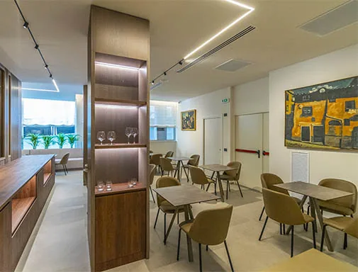 sala dell'hotel con tavoli, sedie, scaffale in legno illuminato e grandi finestre