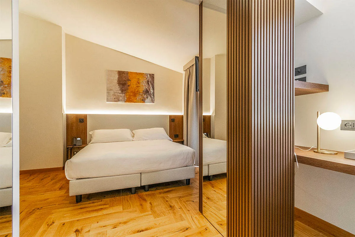 junior suite con letto matrimoniale, pavimento in legno, specchio e scrivania separata da listelli