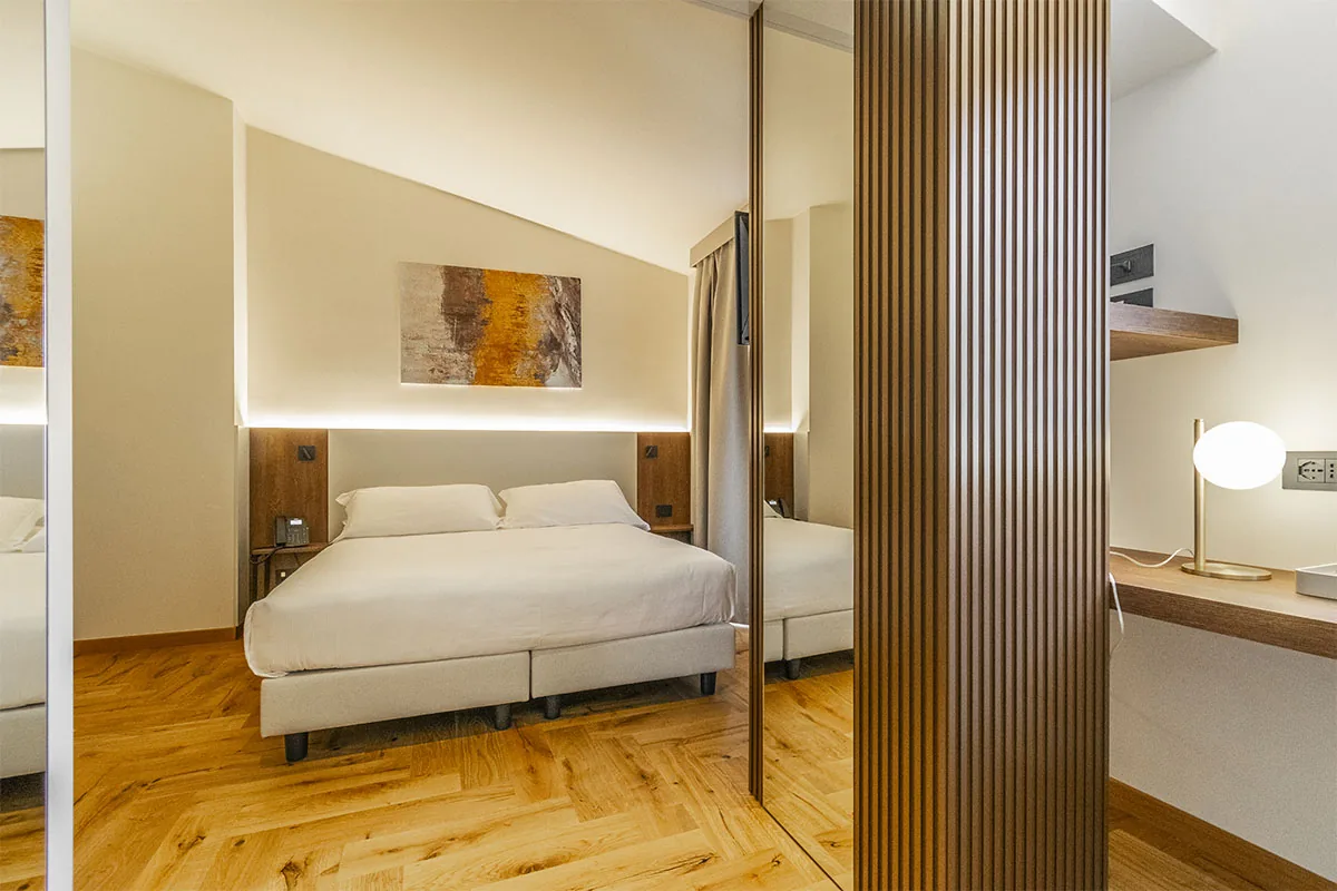 junior suite con letto matrimoniale, parete a specchio, divisorio a listelli e scrivania illuminata