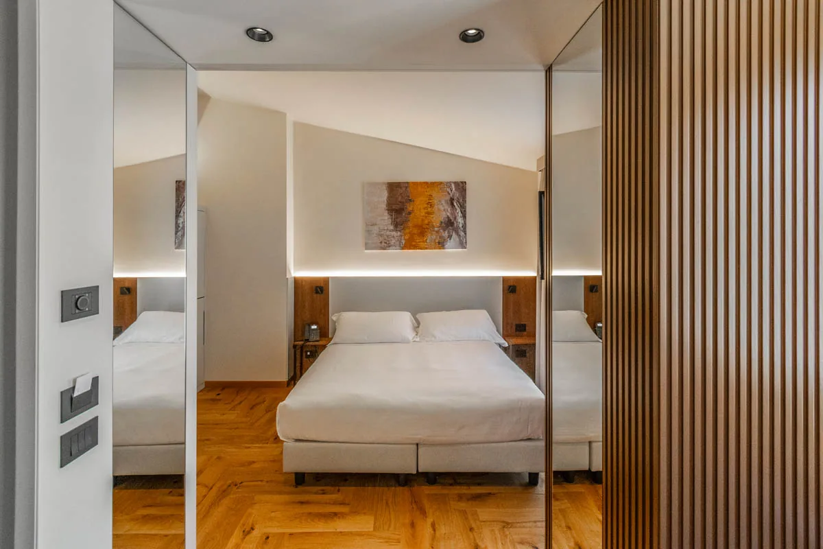 junior suite con letto matrimoniale centrale, specchi laterali e pavimento in legno