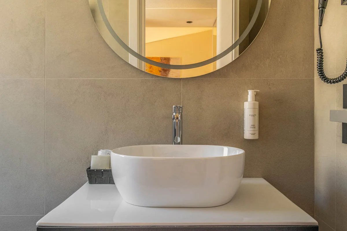 bagno della Junior Suite con lavabo da appoggio, specchio rotondo e parete grigia