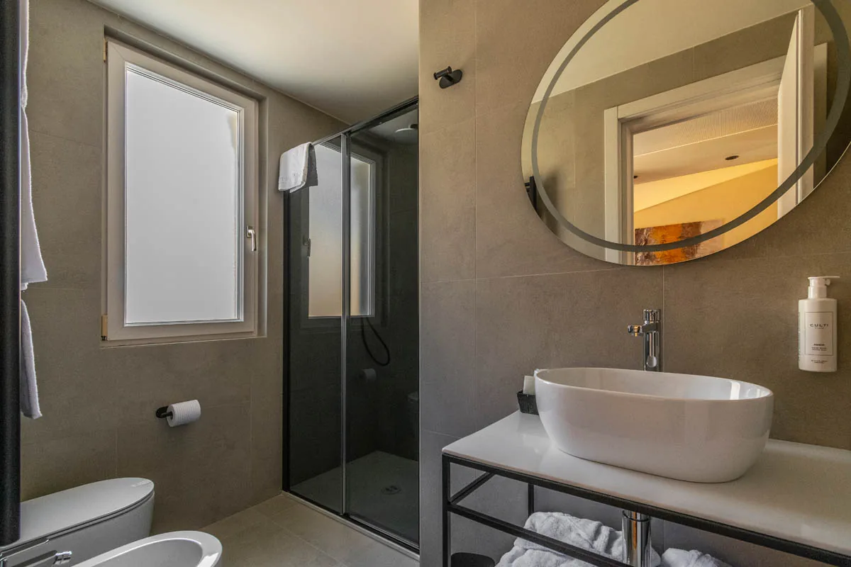 bagno della Junior Suite con doccia vetrata, lavabo ovale, specchio e finestra