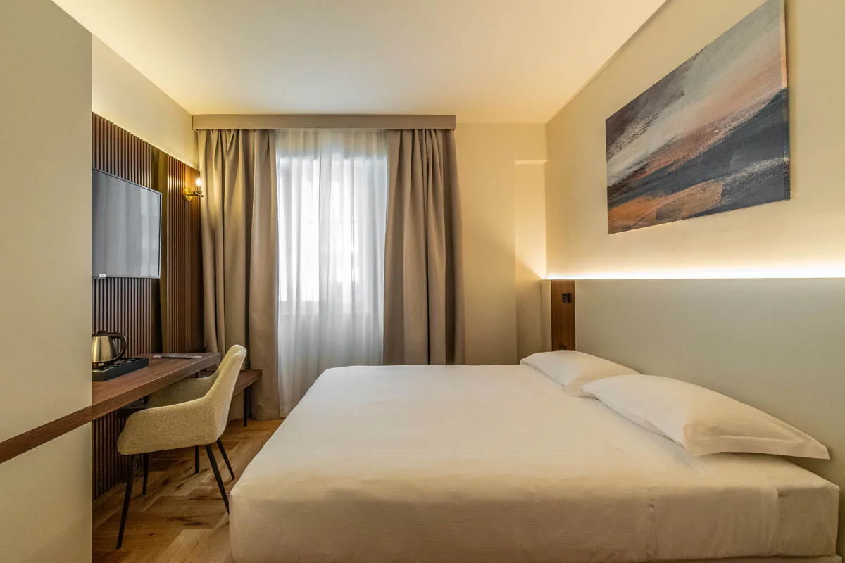 camera Standard con letto matrimoniale, scrivania, finestra con tende e quadro astratto