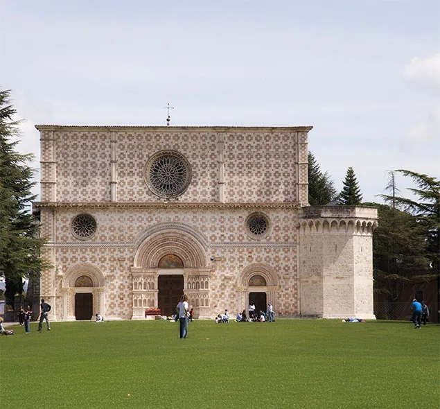 facciata della basilica di Santa Maria di Collemaggio con prato e visitatori
